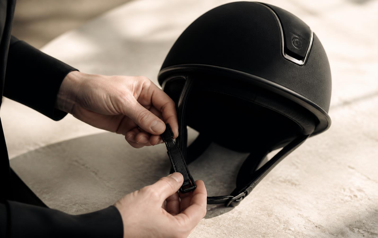 Close detail of a riding hat harness being adjusted by hand during a fitting